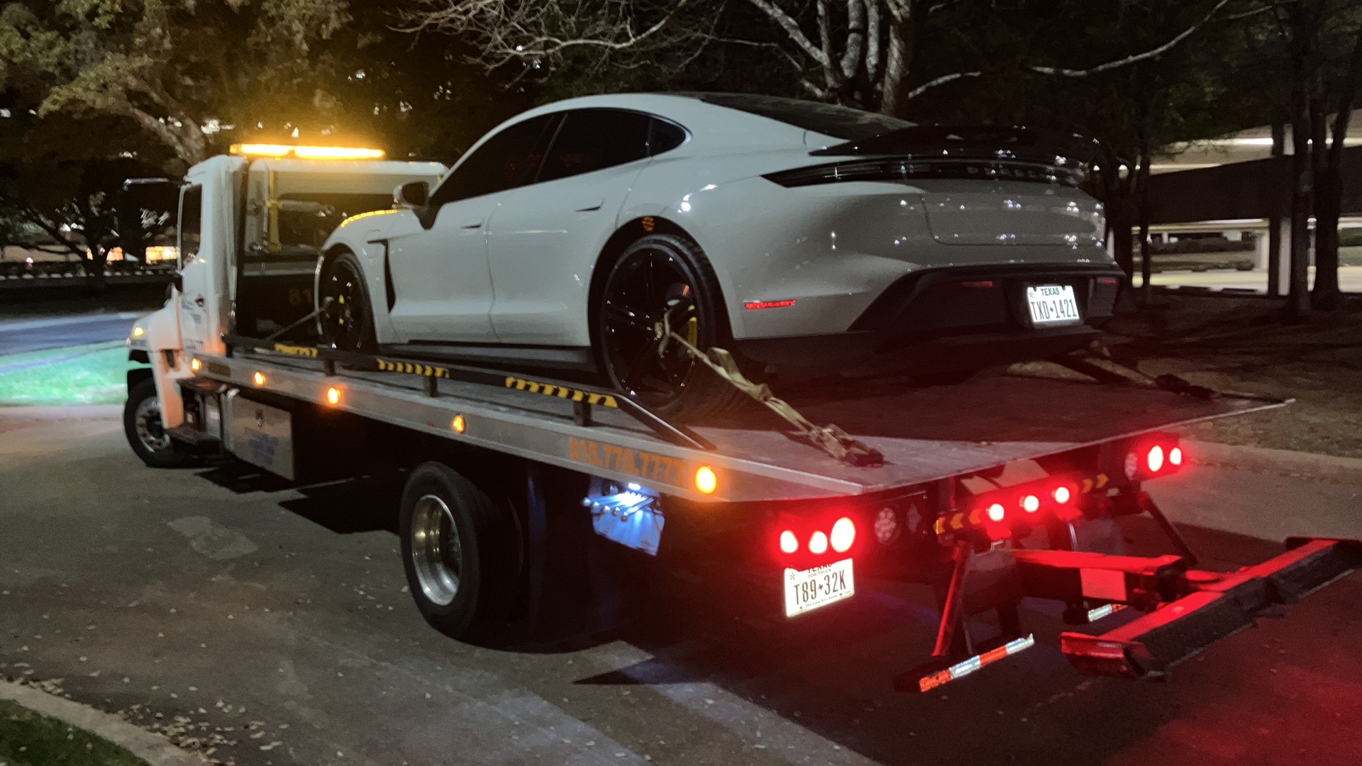 White luxury sports car being towed on a flatbed truck at night