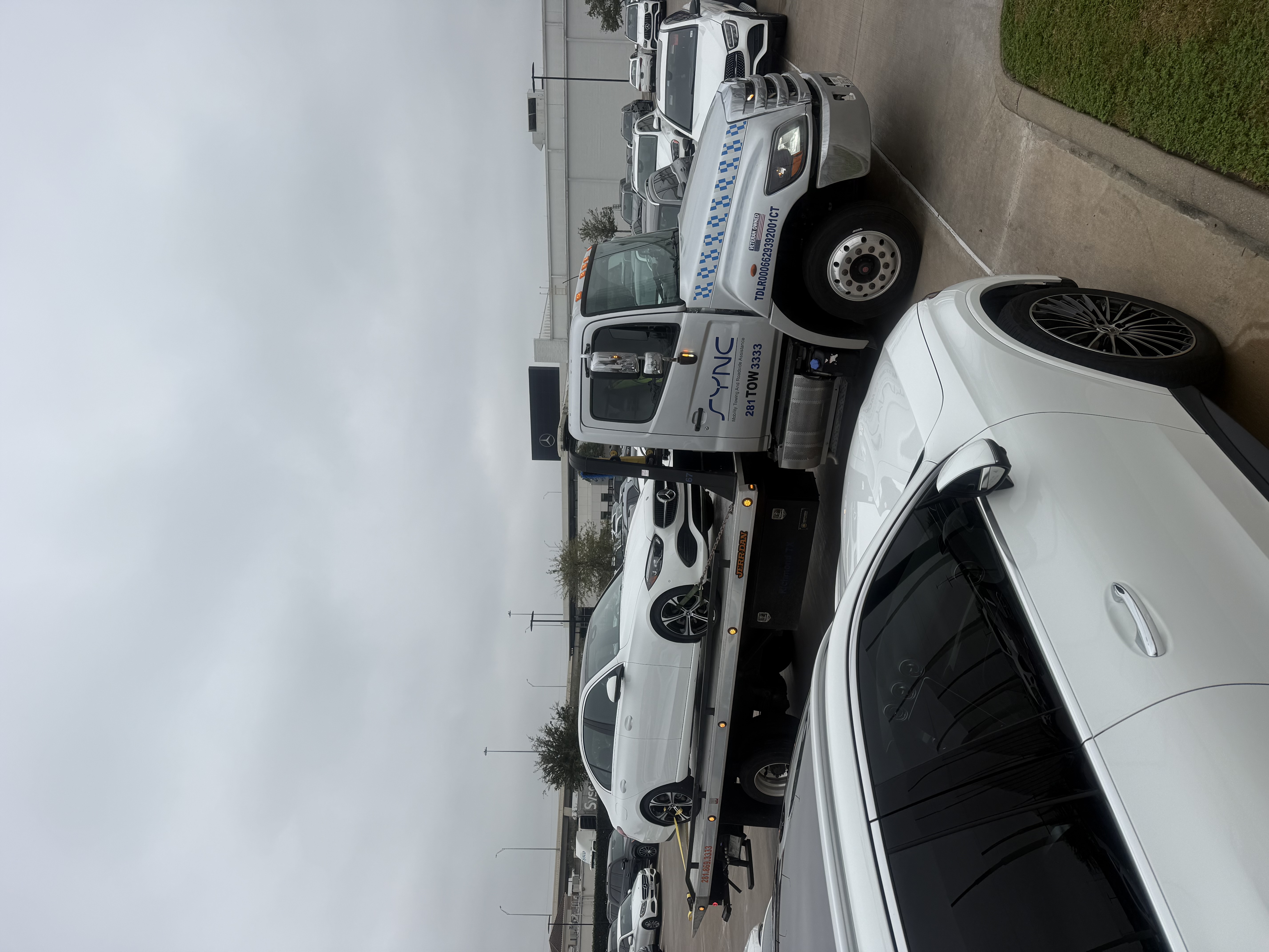 White Mercedes car being towed on a flatbed truck in parking lot