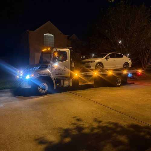 White tow truck loading a car at night with flashing emergency lights