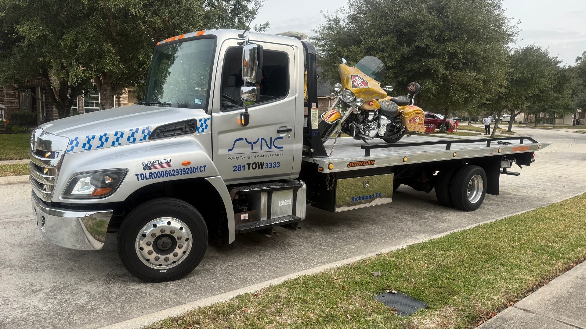 SYNC tow truck transporting a yellow motorcycle on a residential street