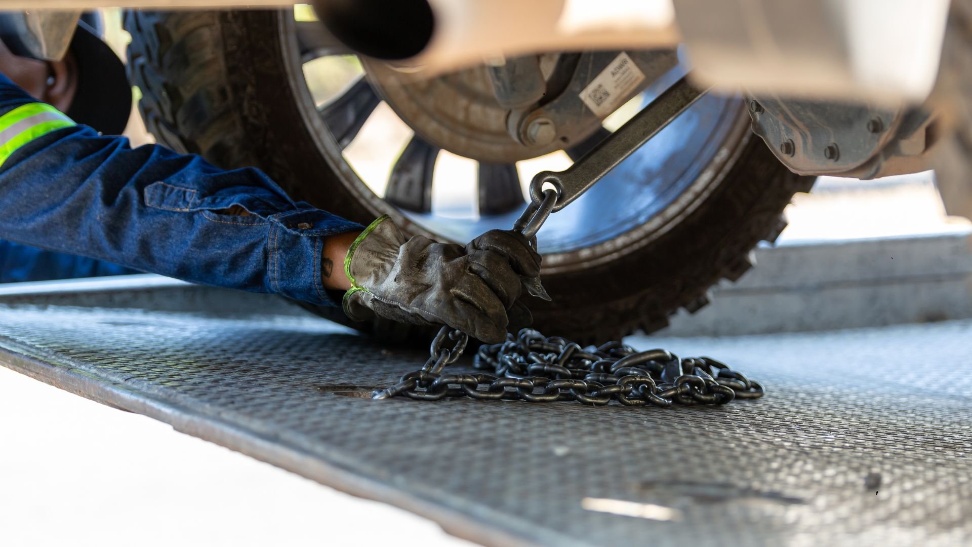 Worker in safety gloves securing heavy chain near vehicle tire