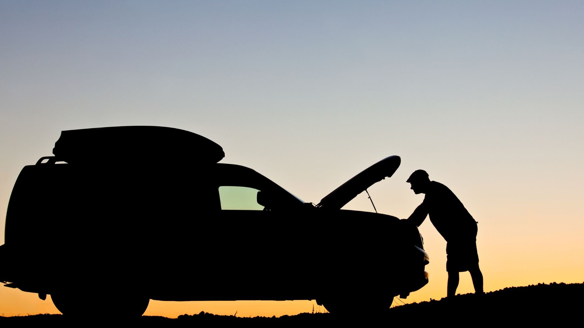 Silhouette of person checking car engine at sunset with roof cargo box