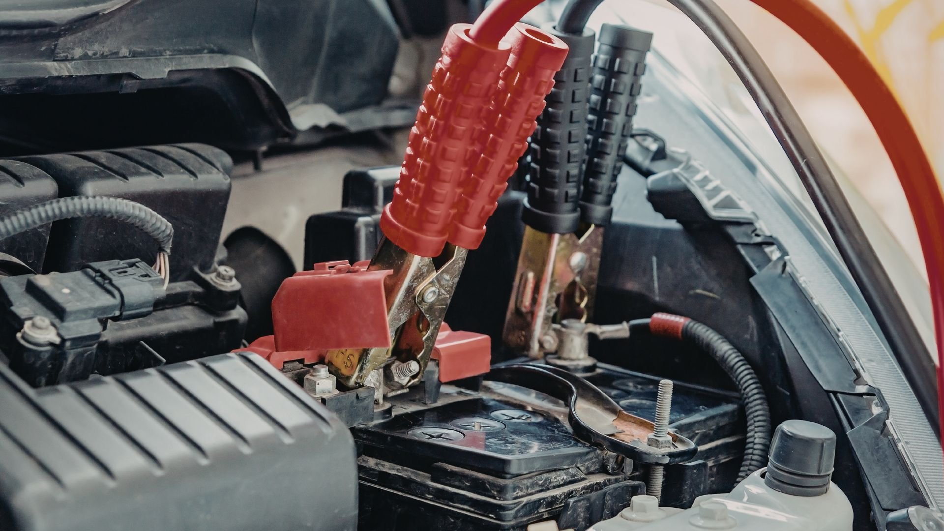 Red battery jumper cables connected to car battery under hood