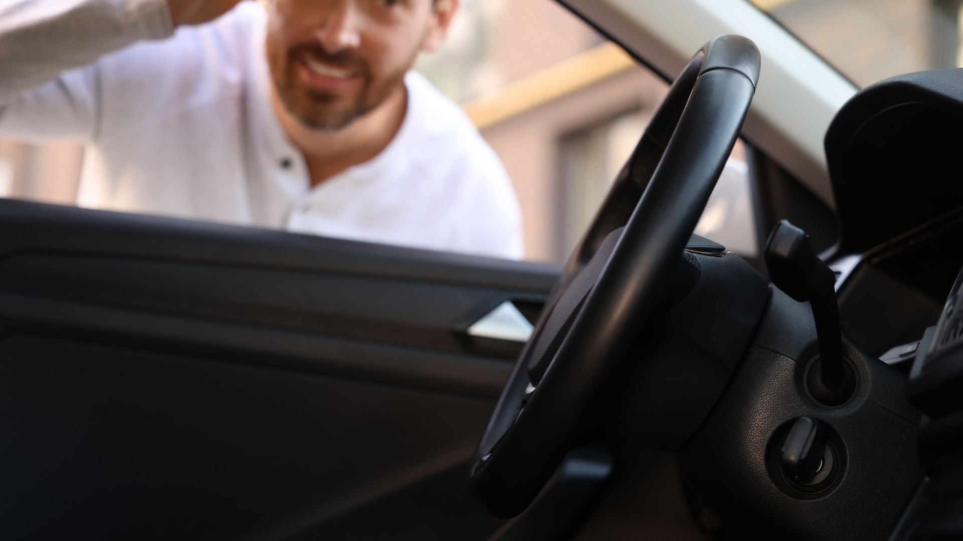 Person in white shirt looking inside car with black steering wheel