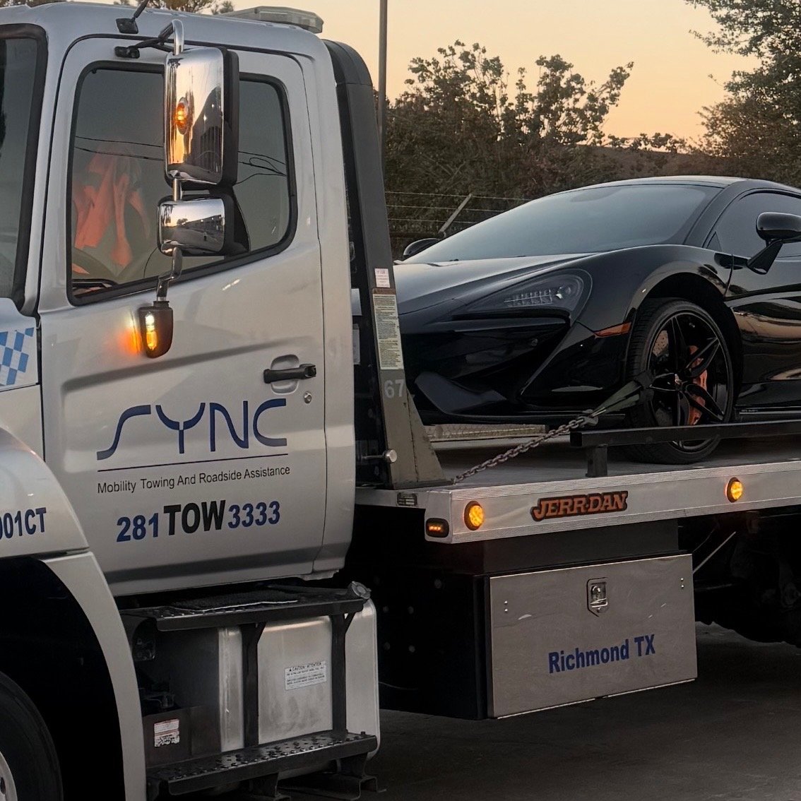 Black sports car being towed by SYNC tow truck at sunset